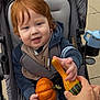 toddler, child, stroller, pumpkin, gourd, hand, reaching, outdoor, pavement, clothing, red_hair, baby, seatbelt, smile, face, person, hoodie, sippy_cup, gray, blue