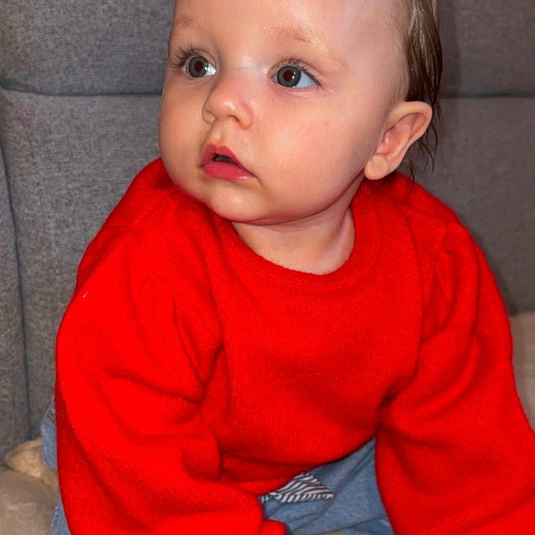 Zalyah participe au concours pour gagner de l'argent avec cette photo : baby, blue_jeans, child, couch, cozy, crawling, curious, cute, expression, face, footwear, furniture, hair_clip, hand, indoors, person, red_sweater, sitting, toddler, young_child