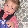 toddler, child, blanket, pink_clothing, face, hand, blue_eyes, pony_tail, cushion, patterned_background, indoor, baby, person, portrait, cozy, soft_texture, cute, snuggled, casual, young_child