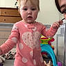 Destiny joined the competition — help win amazing prizes! toddler, child, pink_onesie, polka_dots, heart, standing, toy, indoor, dresser, person, face, curious, baby, playroom, adult_partial, floor, furniture, colorful, cute, home