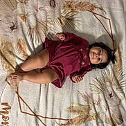 Nevaeh is registered to the contest to win money with this photo: baby, child, infant, blanket, maroon_dress, face, smile, hair, skin, lying_down, soft_texture, floral_pattern, numbers, name, indoors, cute, portrait, young_child, toddler, comfortable