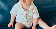 Elias joined the competition — help win amazing prizes! baby, child, infant, sitting, blue_couch, romper, buttoned_clothing, indoor, natural_light, curious_expression, barefoot, face, skin, hair, window, background_blur, soft_light, person, young_child, smile