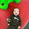 baby, child, smiling, toy, playground, green, red, clothing, happy, infant, person, cute, lying_down, play, colorful, young_child, joyful, indoors, one_person, face