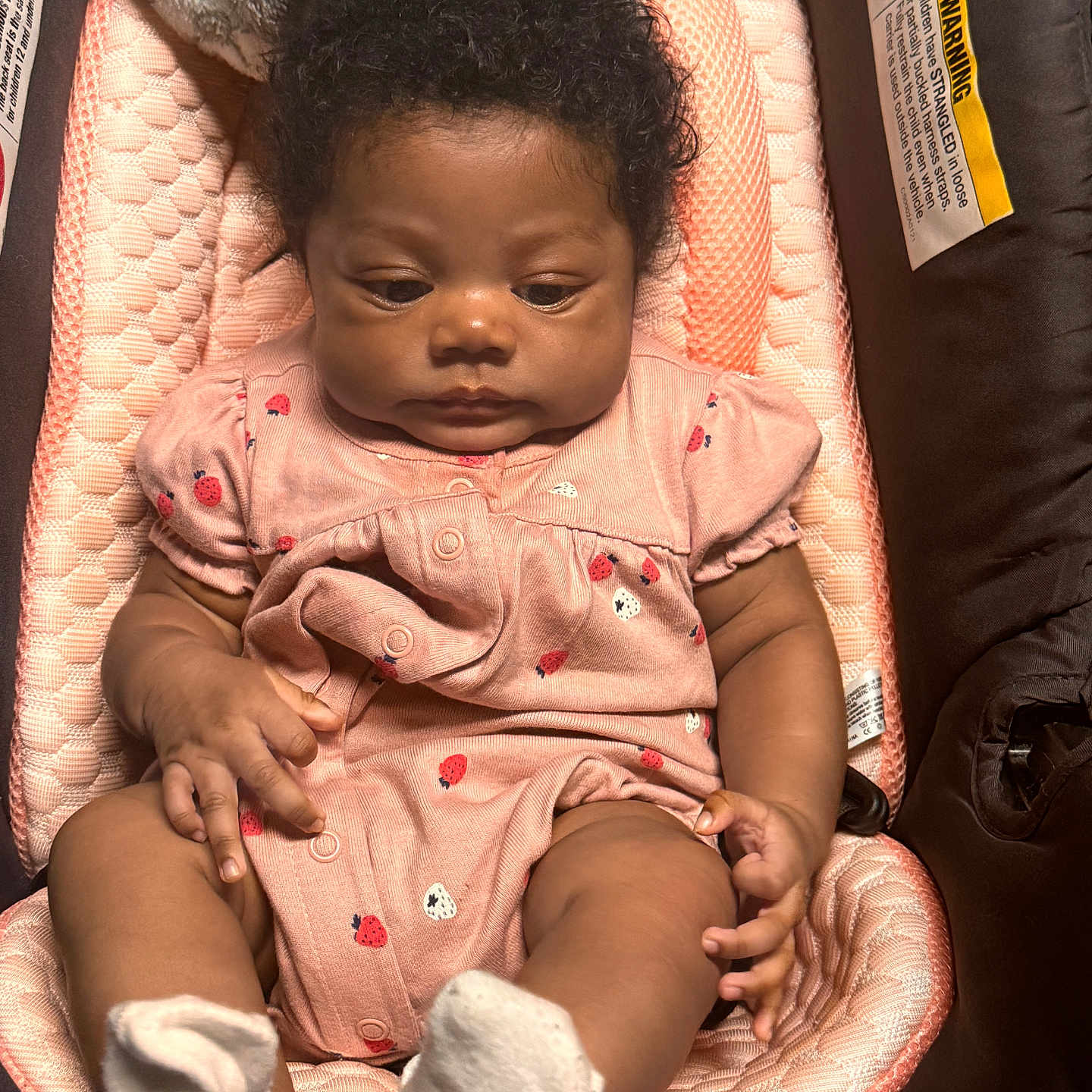 Hosanna is registered to the contest to win money with this photo: baby, car_seat, child, closeup, curly_hair, cushion, cute, expression, hands, indoor, infant, legs, patterned_clothing, person, pink_outfit, seated, skin, socks, soft_lighting, young_child
