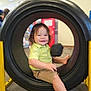 Ethan joined the competition — help win amazing prizes! toddler, child, smiling, tire, indoor, play_area, yellow_shirt, khaki_shorts, sitting, happy, curly_hair, foot, person, toy, blurred_background, playground_equipment, young_child, casual_clothing, fun, framed