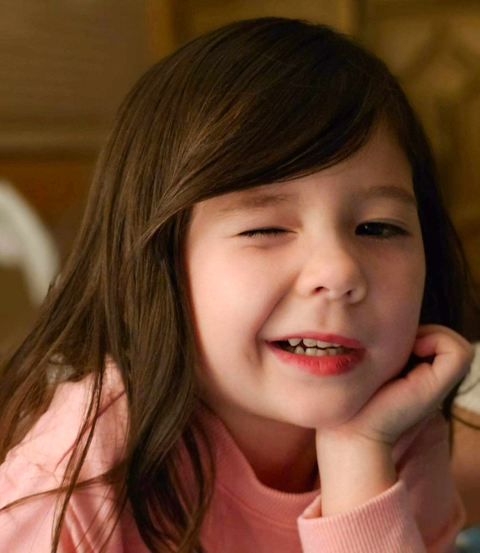 Katherine joined the competition — help win amazing prizes! child, girl, face, winking, smiling, long_hair, brown_hair, pink_sweater, hand, chin, portrait, indoor, cute, happy, resting, young, person, closeup, skin, expression