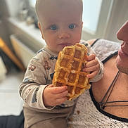 Ange a rejoint le concours — aidez-le/la à gagner de superbes lots ! baby, child, waffle, food, indoor, person, hand, face, blue_eyes, clothing, holding, infant, cute, portrait, expression, adult, comfort, sitting, breakfast, snack