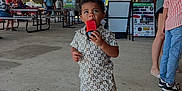 Preston is registered to the contest to win money with this photo: toddler, child, popsicle, food, outdoor, pavilion, people, clothing, shorts, shirt, footwear, white_shoes, concrete_floor, picnic_tables, sign, event, summer, daytime, casual, community