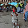 toddler, child, popsicle, food, outdoor, pavilion, people, clothing, shorts, shirt, footwear, white_shoes, concrete_floor, picnic_tables, sign, event, summer, daytime, casual, community