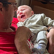 Robin is registered to the contest to win money with this photo: baby, adult, man, smiling, indoor, holding, happy, clothing, glasses, socks, person, portrait, family, love, interaction, casual, home, sitting, cute, affection