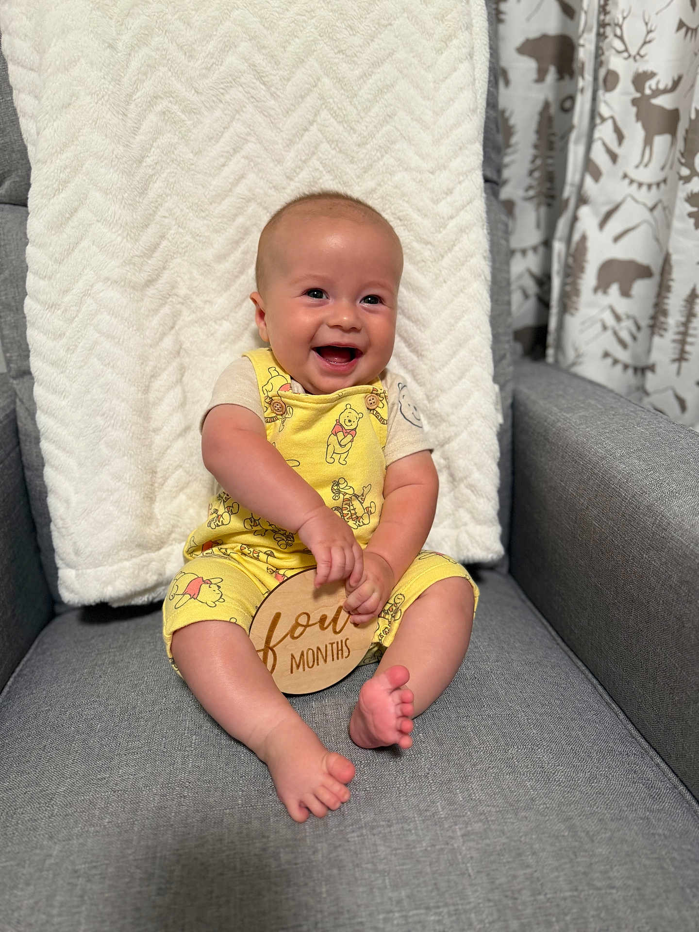 Caleb joined the competition — help win amazing prizes! baby, smiling, sitting, yellow_clothing, winnie_the_pooh, woodland_curtains, gray_armchair, soft_blanket, happy, infant, indoors, cute, child, plush_texture, wooden_sign, four_months, portrait, feet, hands, cozy