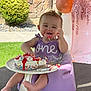 baby, birthday_cake, purple_dress, smiling, face, hand, frosting, sprinkles, outdoor, grass, balloons, decorations, seat, foot, table, celebration, one_year_old, happy, messy, child