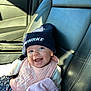 baby, beanie, bib, blanket, car_seat, child, clothing, floral, happy, hat, infant, interior, leather, navy_blue, pink, portrait, seatbelt, smiling, sunlight, window