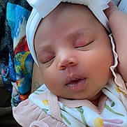 Jehlani is registered to the contest to win money with this photo: baby, sleeping, headband, bow, infant, floral_clothing, arm, tattoo, blanket, closeup, peaceful, cute, skin, portrait, newborn, child, resting, soft, indoors, person