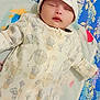 baby, sleeping, onesie, hat, blanket, floral_pattern, teddy_bear, hot_air_balloon, infant, cute, cozy, child, bedtime, resting, soft_fabric, indoors, portrait, newborn, peaceful, baby_clothing
