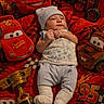 baby, infant, blanket, plush_toy, car_toy, piston_cup, clothing, hat, socks, face, child, lying_down, red_color, animated_characters, disney_cars, smile, toy, soft_toy, indoor, portrait