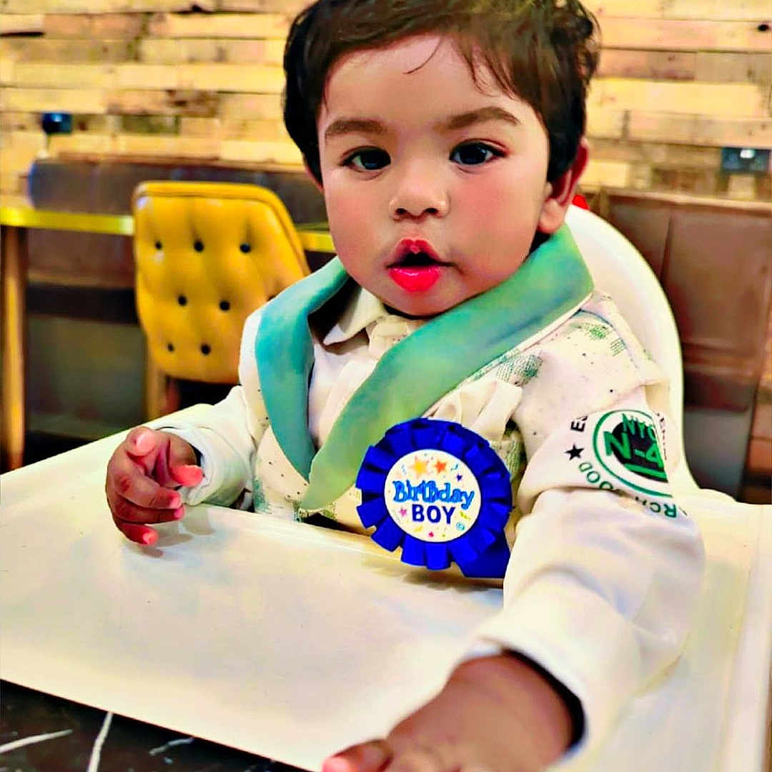 Ekjyot Singh Bhatti is registered to the contest to win money with this photo: badge, birthday_boy, cafe, celebration, chair, child, clothing, curious, face, green_wall, hand, high_chair, indoor, person, portrait, smiling, table, toddler, wooden_panel, young_child