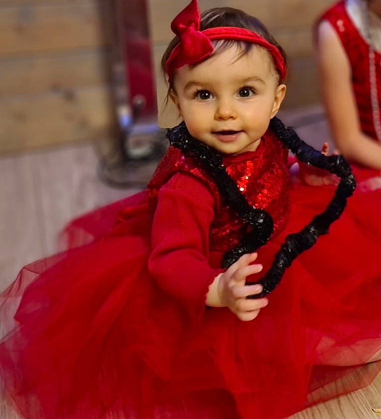 Emma participe au concours pour gagner de l'argent avec cette photo : baby, baby_toddler_clothing, child, dress, event, eye, face, fashion_accessory, fashion_design, formal_wear, hair_accessory, happy, headwear, jewellery, magenta, person, pink, red, skin, sleeve