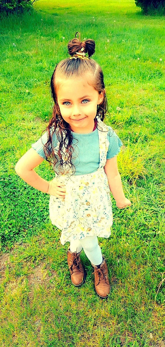 Taylah is registered to the contest to win money with this photo: baby_toddler_clothing, brown_hair, child, day_dress, foot, fun, gesture, grass, grass_family, grassland, green, happy, joy, meadow, pattern, people_in_nature, person, plant, sandal, skin