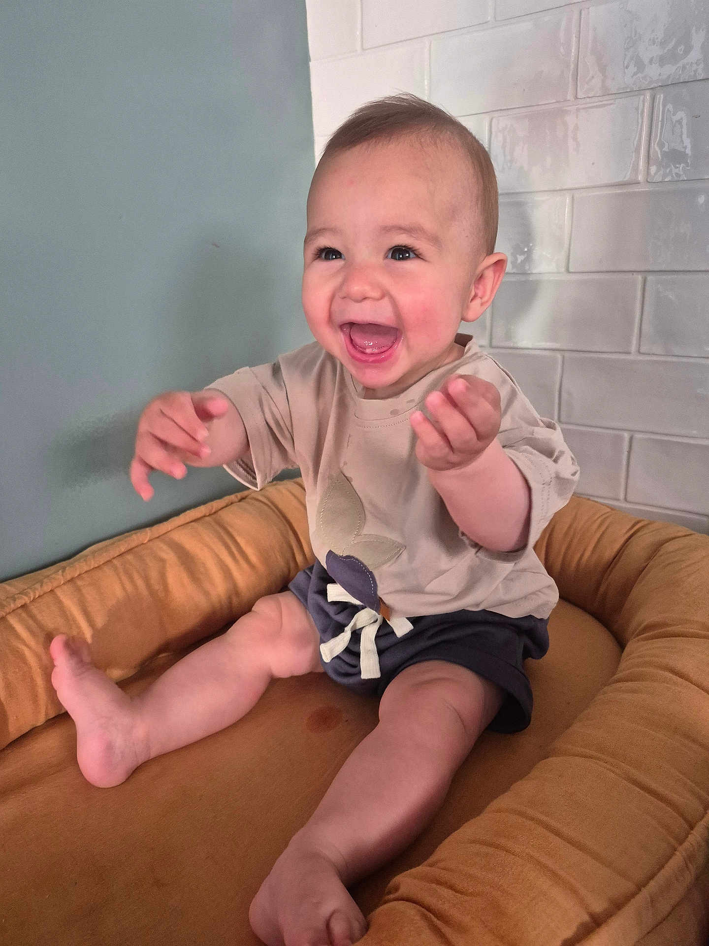 Achille a rejoint le concours — aidez-le/la à gagner de superbes lots ! baby, child, smiling, happy, sitting, cushion, seat, indoor, clothing, shorts, tshirt, face, hands, legs, foot, head, baby_furniture, tile_wall, light, expression
