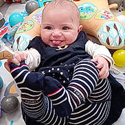 Zuleyha a rejoint le concours — aidez-le/la à gagner de superbes lots ! baby, infant, play_mat, toy, stuffed_animal, ball, striped_clothing, smiling, tongue_out, cute, child, floor, playpen, colorful, soft_toy, happy, indoors, person, legs, hands