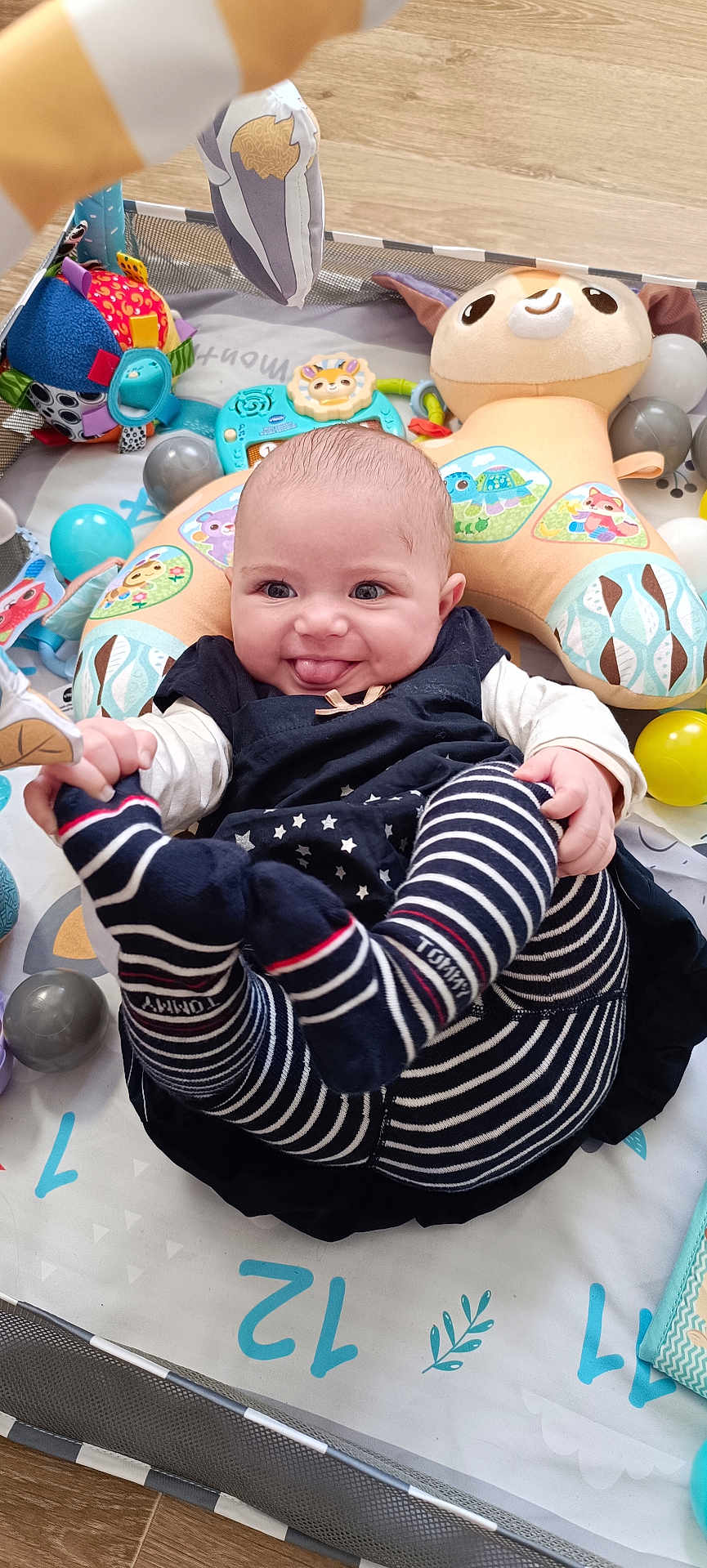 Zuleyha a rejoint le concours — aidez-le/la à gagner de superbes lots ! baby, infant, play_mat, toy, stuffed_animal, ball, striped_clothing, smiling, tongue_out, cute, child, floor, playpen, colorful, soft_toy, happy, indoors, person, legs, hands