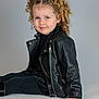 Milaya a rejoint le concours — aidez-le/la à gagner de superbes lots ! black_clothing, blue_eyes, casual_pose, child, confident, curly_hair, cute, fashion, girl, indoor, leather_jacket, minimalist, person, pigtails, portrait, sitting, smile, studio_background, white_surface, young
