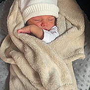 Nino participe au concours pour gagner de l'argent avec cette photo : baby, newborn, sleeping, blanket, beige_blanket, white_hat, swaddle, arm, hand, face, portrait, cozy, soft_texture, cushion, seat, indoors, knit_hat, infant, peaceful, nursery