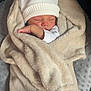 baby, newborn, sleeping, blanket, beige_blanket, white_hat, swaddle, arm, hand, face, portrait, cozy, soft_texture, cushion, seat, indoors, knit_hat, infant, peaceful, nursery