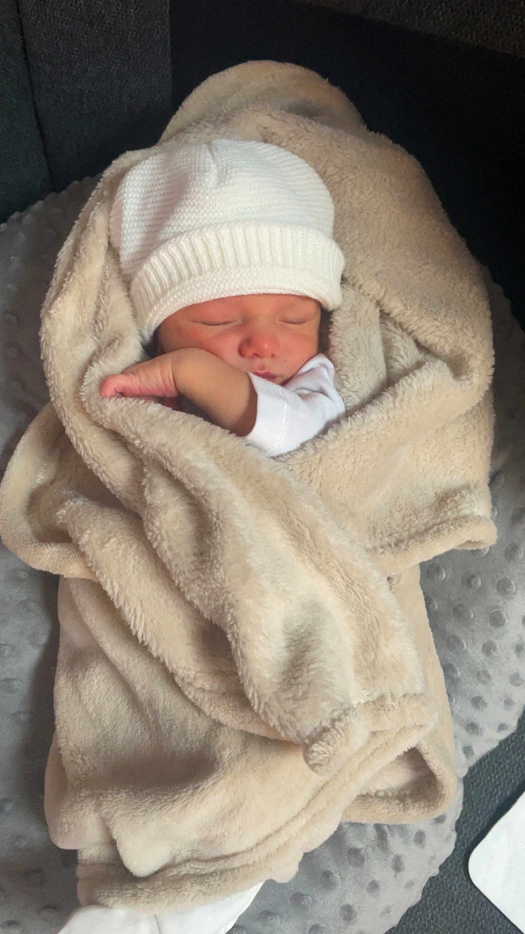 Nino participe au concours pour gagner de l'argent avec cette photo : baby, newborn, sleeping, blanket, beige_blanket, white_hat, swaddle, arm, hand, face, portrait, cozy, soft_texture, cushion, seat, indoors, knit_hat, infant, peaceful, nursery