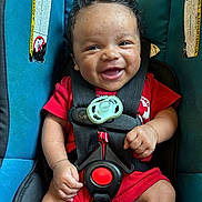 Isaiah is registered to the contest to win money with this photo: baby, infant, child, smiling, happy, portrait, car_seat, safety_harness, pacifier, red_clothing, seated, indoor, close_up, face, eyes, hands, legs, automotive, travel, safety
