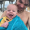 baby, infant, adult, smiling, happy, portrait, beach, outdoor, towel, turquoise, yellow_clothing, wet_hair, bare_shoulders, bridge, concrete, architecture, waterfront, closeup, family, sunny_day