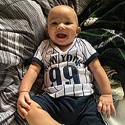 Kasey is registered to the contest to win money with this photo: baby, bed, bedding, blanket, child, clothing, face, hands, happy, home, indoors, infant, legs, portrait, shorts, sitting, smiling, sock, sports_jersey, striped_fabric