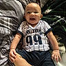 baby, bed, bedding, blanket, child, clothing, face, hands, happy, home, indoors, infant, legs, portrait, shorts, sitting, smiling, sock, sports_jersey, striped_fabric