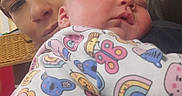 Athena joined the competition — help win amazing prizes! adult, animal_print, baby, child, closeup, clothing, comfort, couch, face, head, holding, indoor, onesie, person, rainbow, rest, skin, sleeping, tenderness, warmth