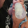 adult, baby, black_shirt, blue_clothes, bottle, care, closeup, clothing, face, feeding, hand, holding, indoor, infant, love, milk, nourishment, person, portrait, skin