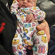 Athena is registered to the contest to win money with this photo: adult, animal_print, baby, clothing, comfort, cozy, cute, hand, holding, indoor, infant, onesie, pattern, peaceful, person, rainbow, relaxing, sleeping, soft, toddler