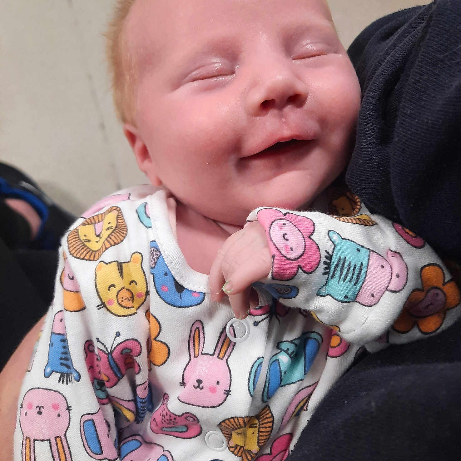 Athena is registered to the contest to win money with this photo: baby, infant, smile, sleeping, onesie, animal_print, cute, cozy, child, hand, face, person, soft_lighting, close_up, newborn, apparel, pattern, adorable, comfort, toddler