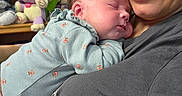 Zoey is registered to the contest to win money with this photo: newborn, baby, infant, parent, adult, sleeping, cuddling, portrait, smiling, glasses, nose_ring, onesie, clothing, stuffed_animals, toys, shelf, nursery, indoor, family, closeup