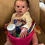 baby, child, infant, bucket, snacks, toys, armchair, socks, clothing, curious, indoor, person, toddler, nutrition_facts, container, seat, pink, hand, expression, couch