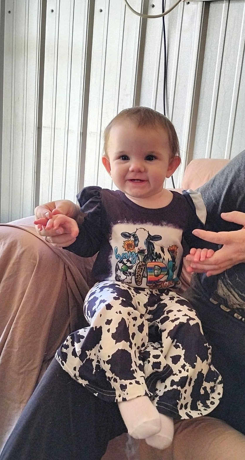 Kinsley is registered to the contest to win money with this photo: toddler, child, smiling, cow_print, clothing, sitting, indoor, person, hands, sofa, blanket, happy, cute, portrait, baby, face, head, adult, holding_hands, cozy