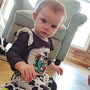 Kinsley joined the competition — help win amazing prizes! toddler, child, indoors, kneeling, cow_print_pants, shirt, toy, floor, window, armchair, curious, person, young_child, home, daylight, wooden_floor, casual_clothing, expression, furniture, playful