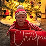 baby, child, christmas, holiday, festive, red_clothing, striped_sleeves, hat, pom_pom, pillow, merry_christmas, carpet, tree, ornaments, lights, indoor, smiling, cute, celebration, seasonal