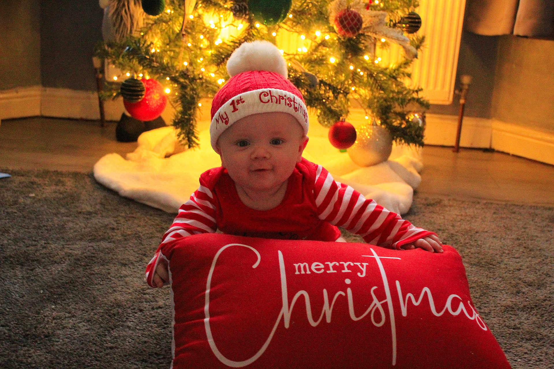 Austin joined the competition — help win amazing prizes! baby, child, christmas, holiday, festive, red_clothing, striped_sleeves, hat, pom_pom, pillow, merry_christmas, carpet, tree, ornaments, lights, indoor, smiling, cute, celebration, seasonal