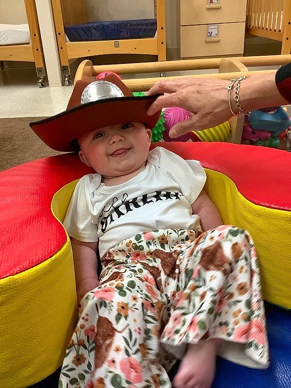 Presley is registered to the contest to win money with this photo: baby, cabinetry, child, comfort, cowboy_hat, event, fashion_accessory, fun, happy, hat, headwear, human_leg, joy, leisure, person, room, sitting, smile, sun_hat, t_shirt
