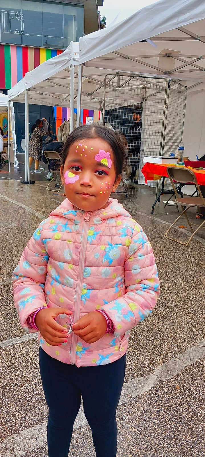 Elsha a rejoint le concours — aidez-le/la à gagner de superbes lots ! child, girl, face_paint, pink_jacket, outdoor, market, tent, colorful, flowers, face, person, pavement, people, event, winter_clothing, standing, cute, casual, festival, fun