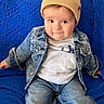 toddler, child, denim_jacket, beanie, blue_couch, sitting, casual_clothing, indoor, curious_expression, smile, jeans, white_shirt, portrait, baby, young_child, fashion, home_interior, cute, cozy, seated