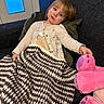 blanket, cardigan, casual_clothing, child, comfort, couch, cozy, furniture, home, indoor, knit_blanket, person, pillow, pink, plush_toy, relaxed, seated, soft, toy, young_child