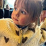 blue_eyes, candid, casual_clothing, child, cozy, curly_hair, cute, expression, face, fluffy_jacket, heart_pattern, indoor, light_brown_hair, looking_away, person, portrait, soft_light, warm_tone, young_child, zipper