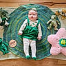baby, infant, teddy_bear, plush_toy, crocheted_blanket, flower_pillow, headband, wooden_floor, green_clothing, white_tights, milestone_marker, four_months, child, floor, toy, cute, lying_down, indoors, portrait, soft_toys